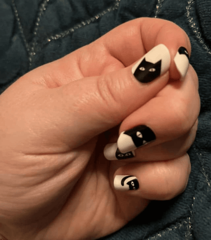 White and black cat nail art wraps on hand showing cute feline faces