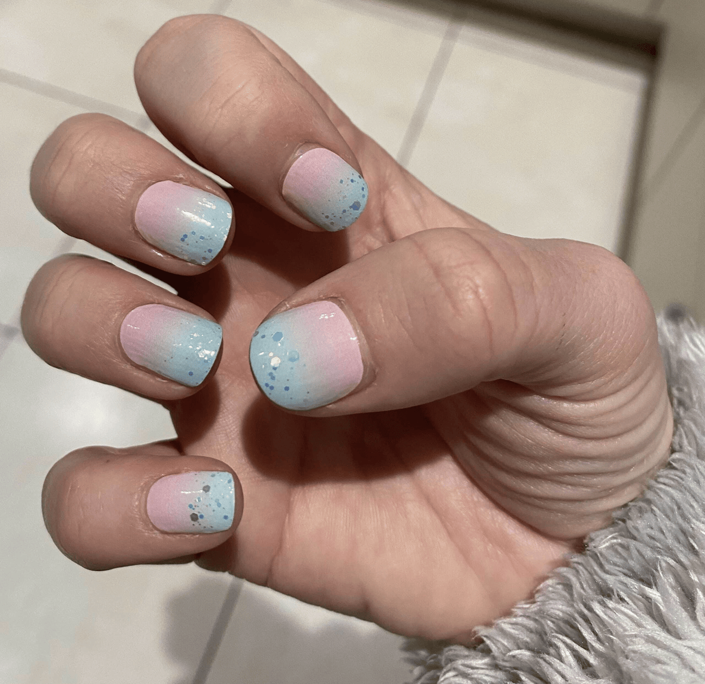Hand wearing pastel blue pink glitter nail wraps with sparkly gradient finish