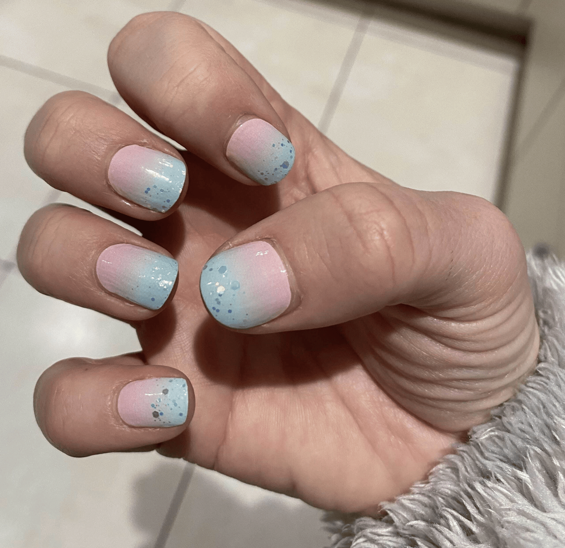 Hand wearing pastel blue pink glitter nail wraps with sparkly gradient finish