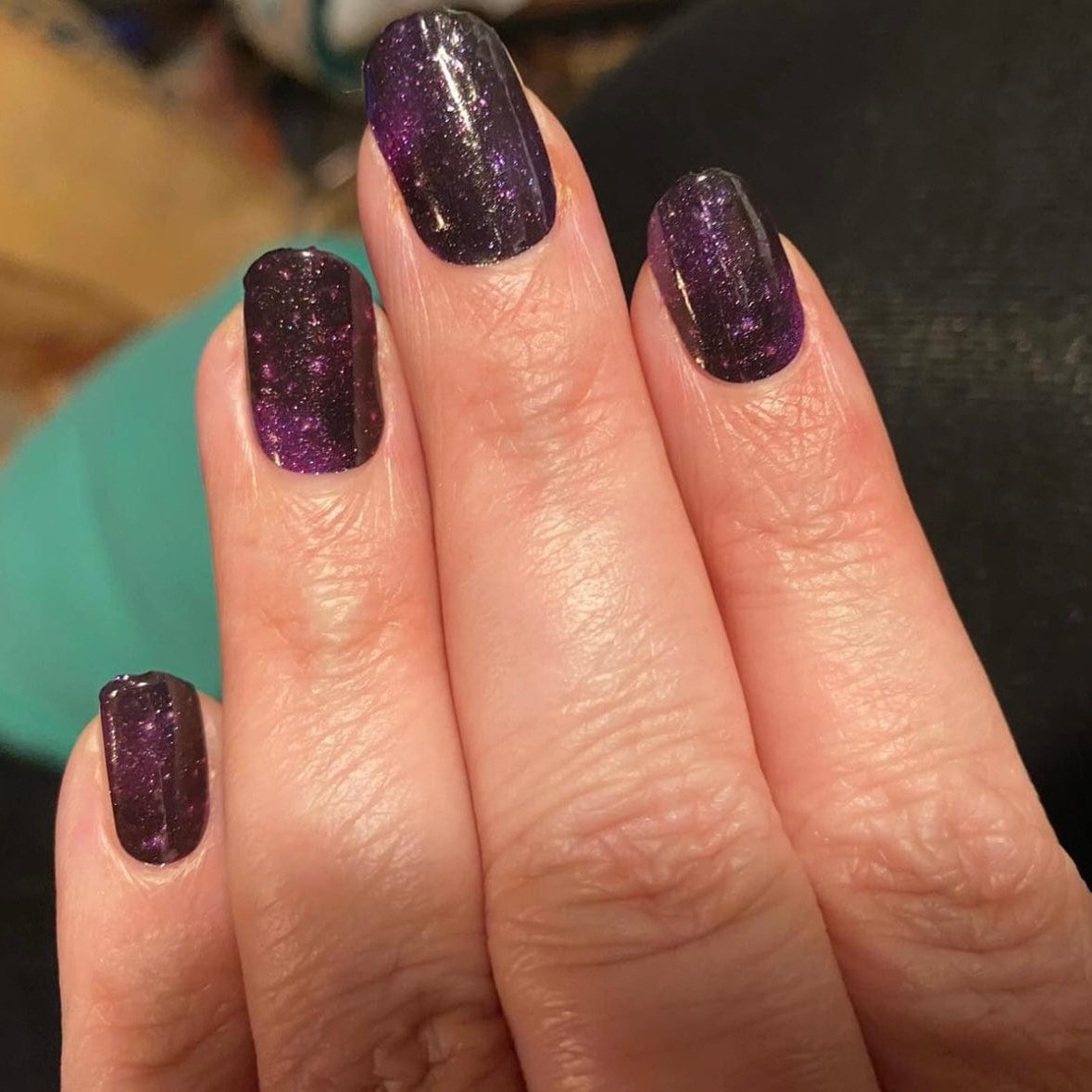 Purple glittery nail wraps on hand displaying cosmic star pattern at-home manicure