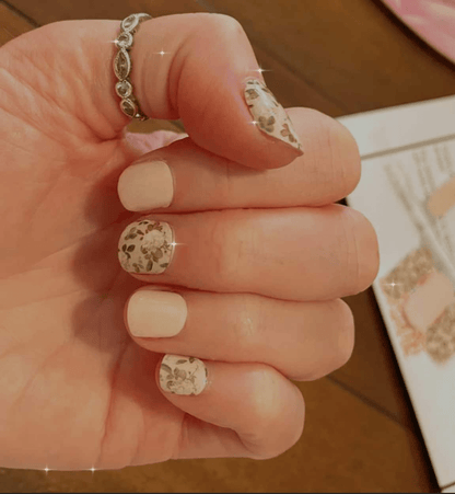 Hand showcasing botanical nail wraps with pink roses and green leaves on nude base