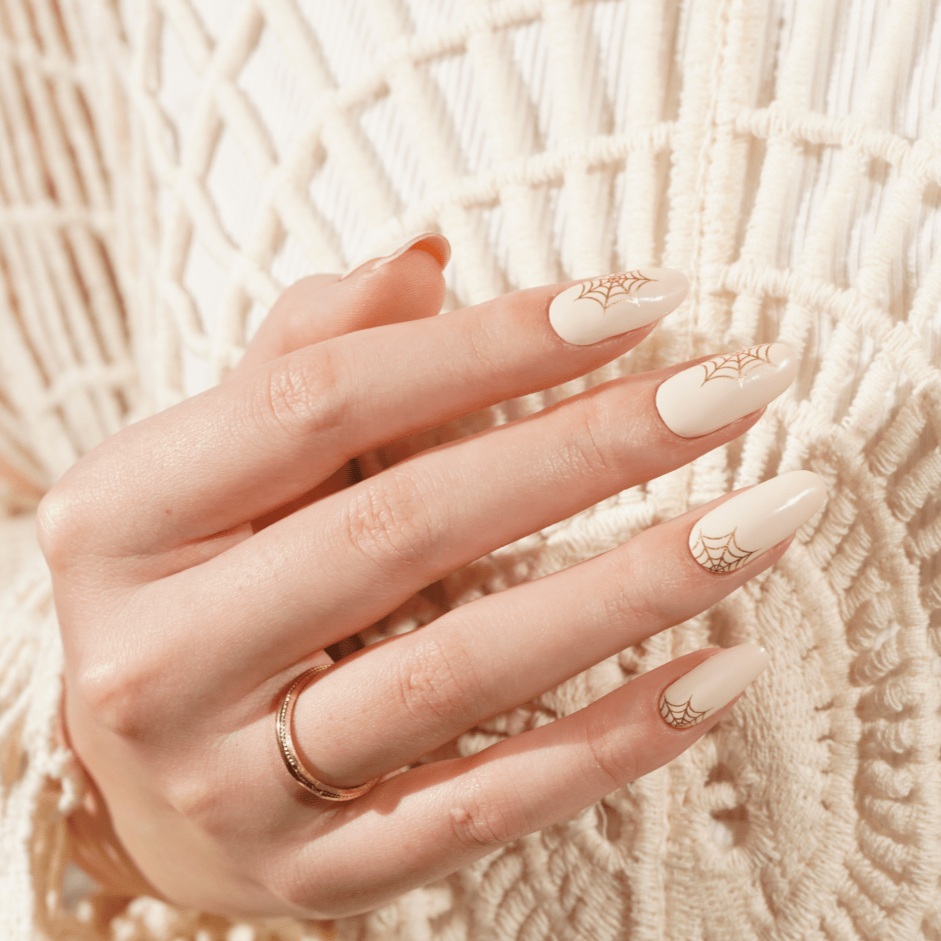 Hand wearing nude nail wraps with gold Gothic lettering nail art design