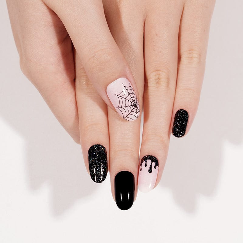 Manicured nails with Halloween nail wraps featuring black glitter and pink spider web art