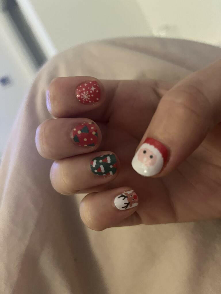 Festive nail art on fingers featuring Santa Claus, reindeer and red green Christmas patterns