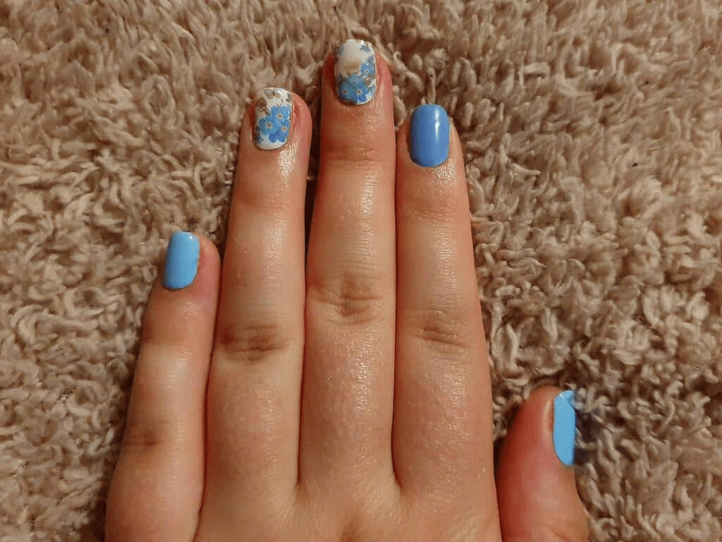 Blue nail wraps with white daisy floral pattern on hand showing spring nail art manicure