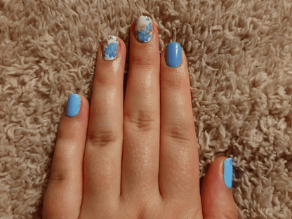 Blue nail wraps with white daisy floral pattern on hand showing spring nail art manicure