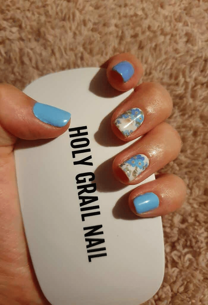 Blue and white daisy nail wraps on hand with product packaging showing floral nail art