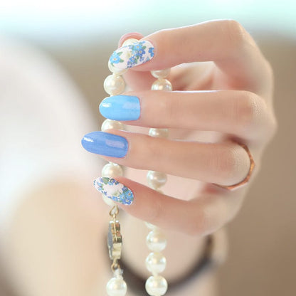 Hand wearing blue floral nail wraps with white daisy pattern gel nail art