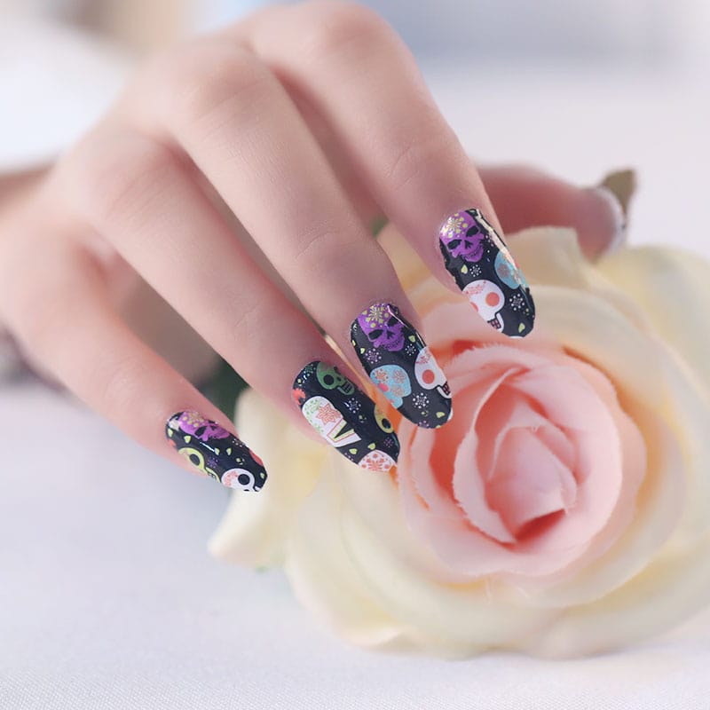 Dia de los Muertos nail art wraps featuring sugar skulls and flowers on manicured hand