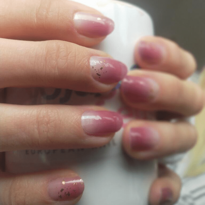 Pink gradient gel nail wraps with glitter accents on hands at-home manicure
