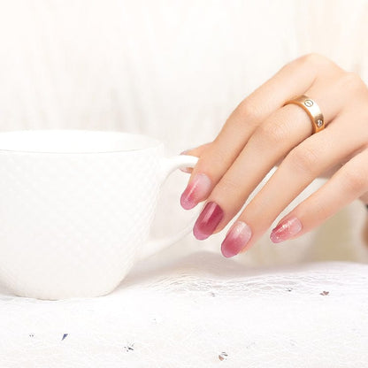 Pink shimmer nail wraps manicure on hand with wine glass
