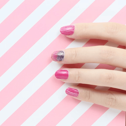Hand wearing pink nail wraps with glitter accent nail against striped background showing geometric design