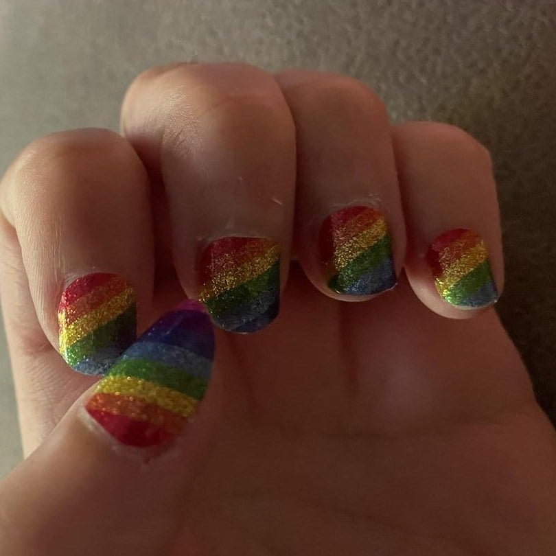 Rainbow glitter nail wraps on hand showing diagonal stripe pattern for pride manicure