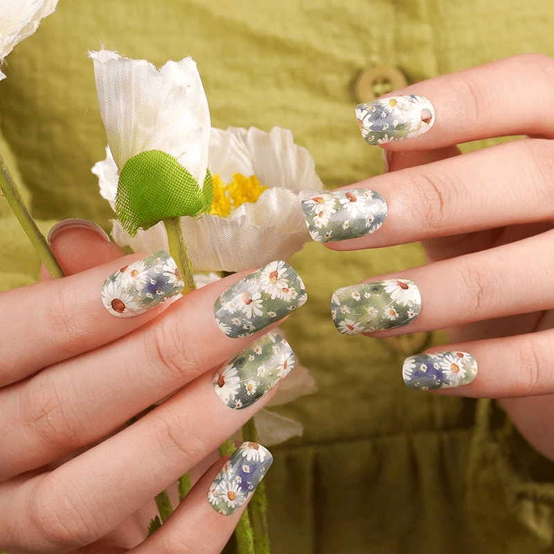 Sage green daisy floral nail wraps on hands holding white flower for spring manicure
