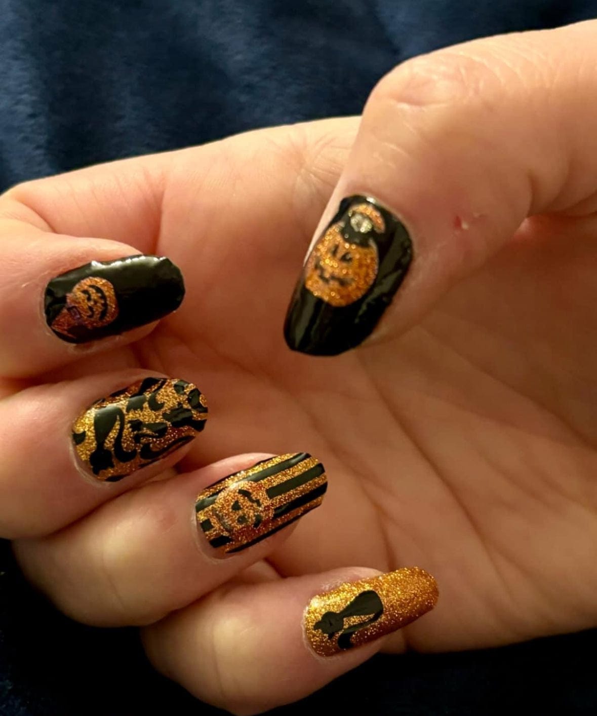 Halloween gel nail wraps on hand with orange glitter pumpkins and black gothic designs