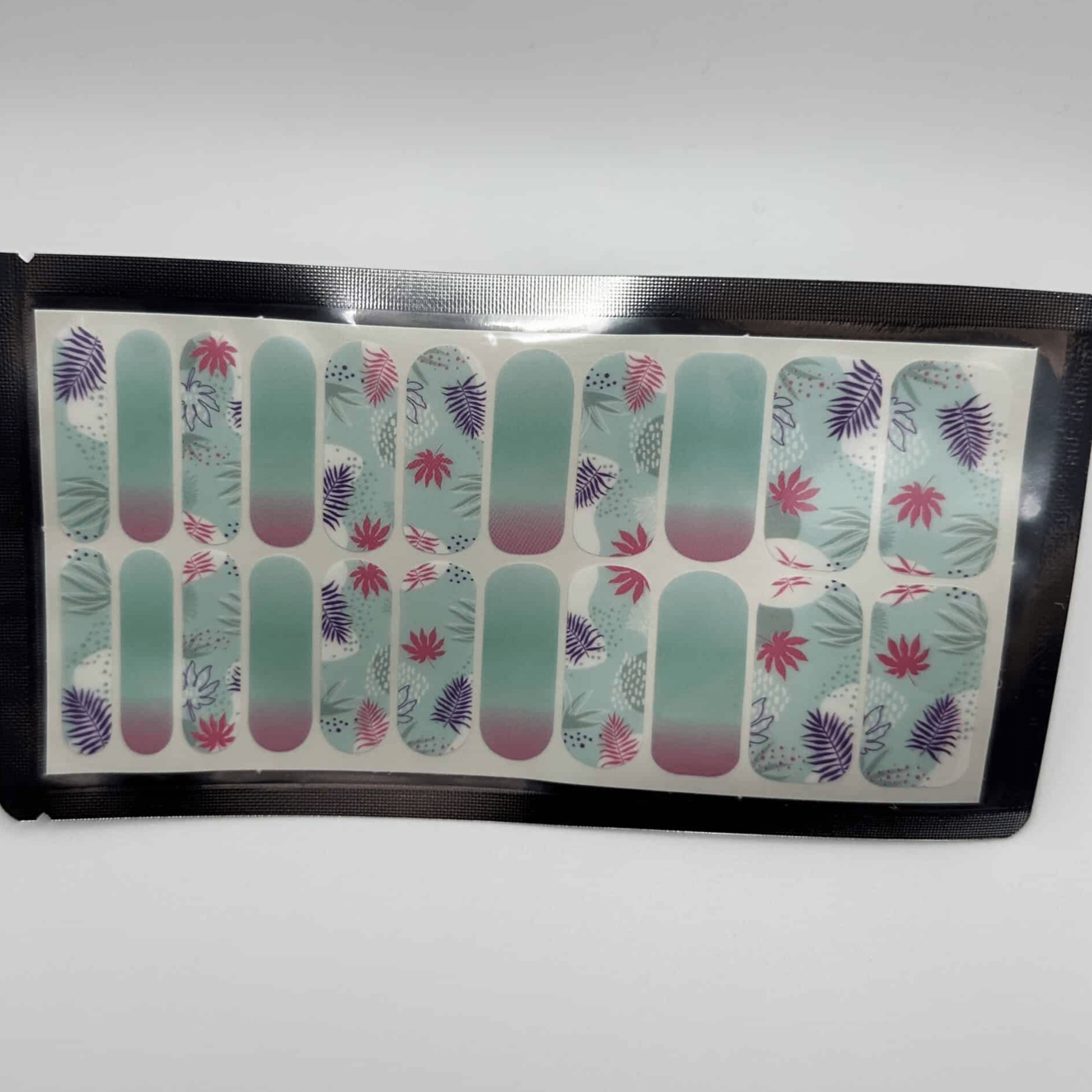 Sheet of tropical nail wraps showing turquoise base with coral and purple palm leaf designs