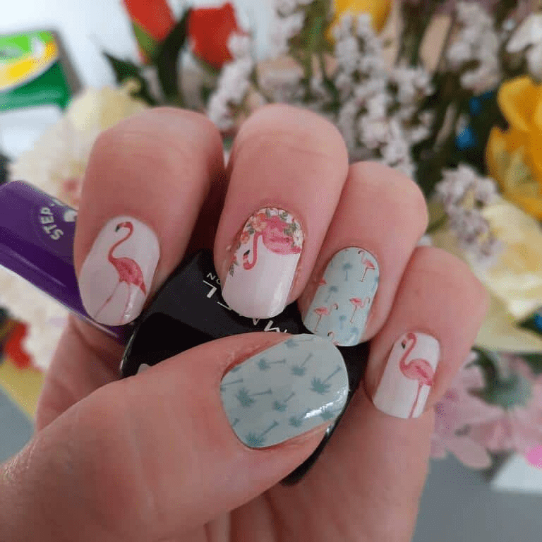 Hand wearing flamingo nail art wraps with pink coral and mint green tropical patterns