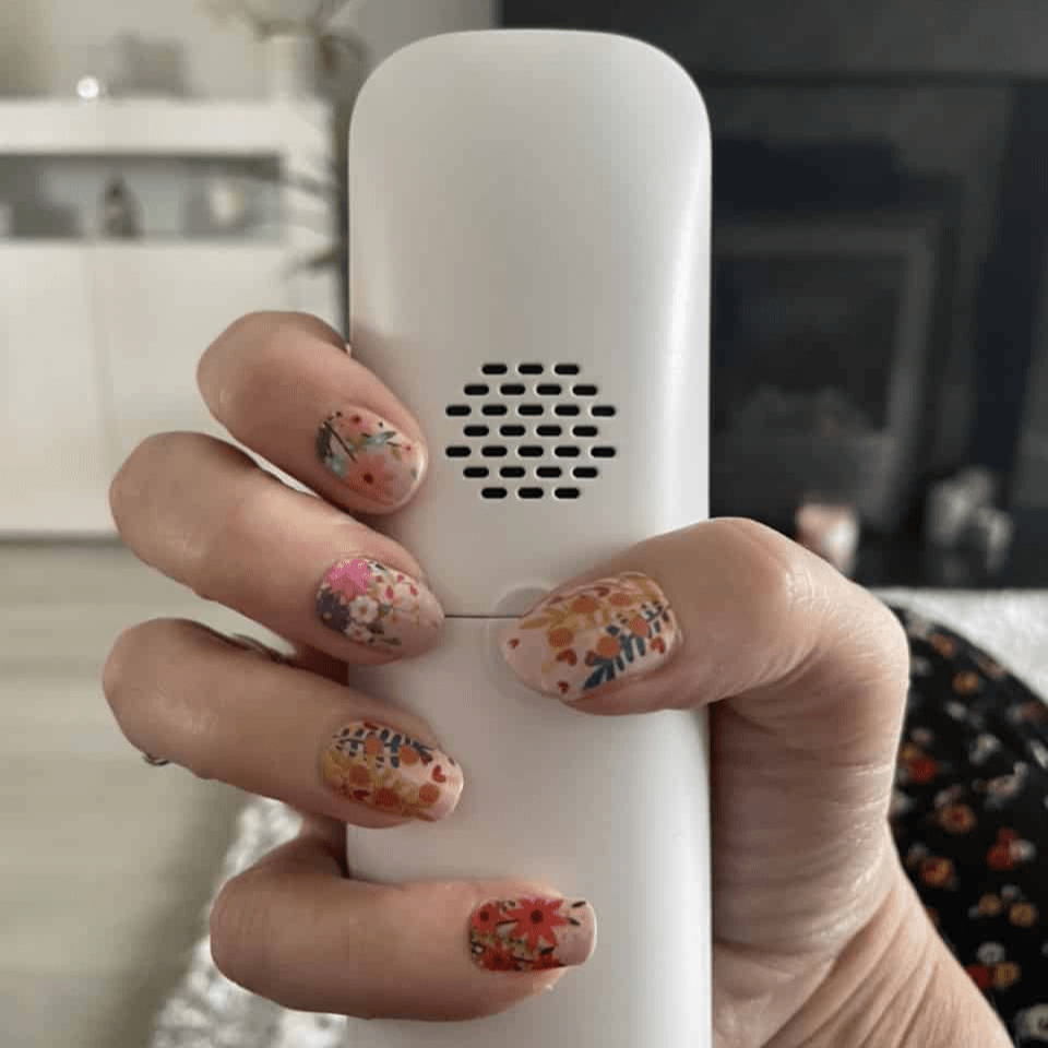 Hand holding white nail file wearing pink floral nail wraps with botanical design