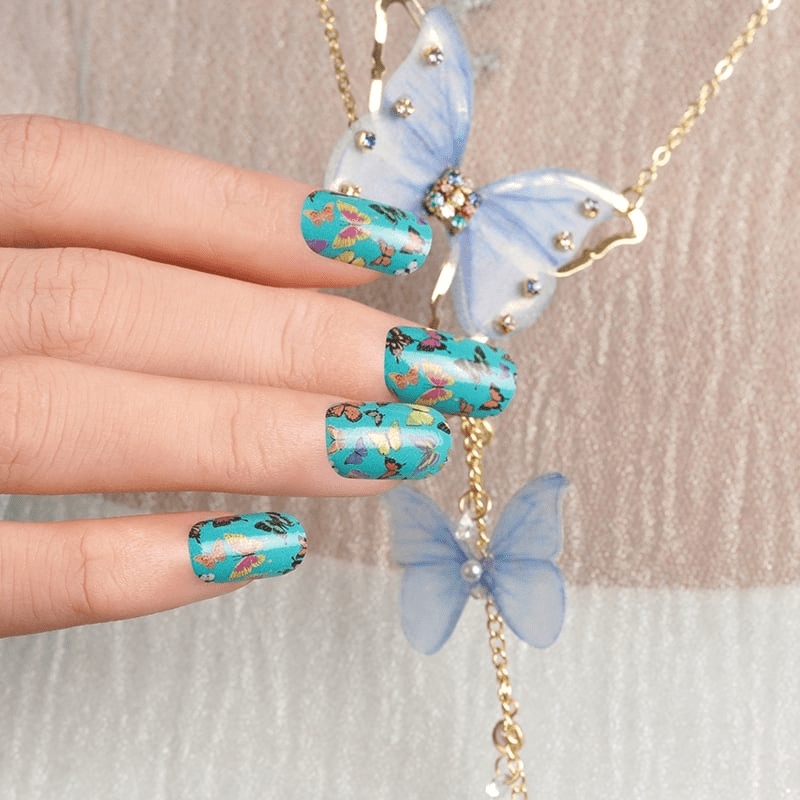 Hand wearing turquoise butterfly nail wraps with blue jewellery accessories