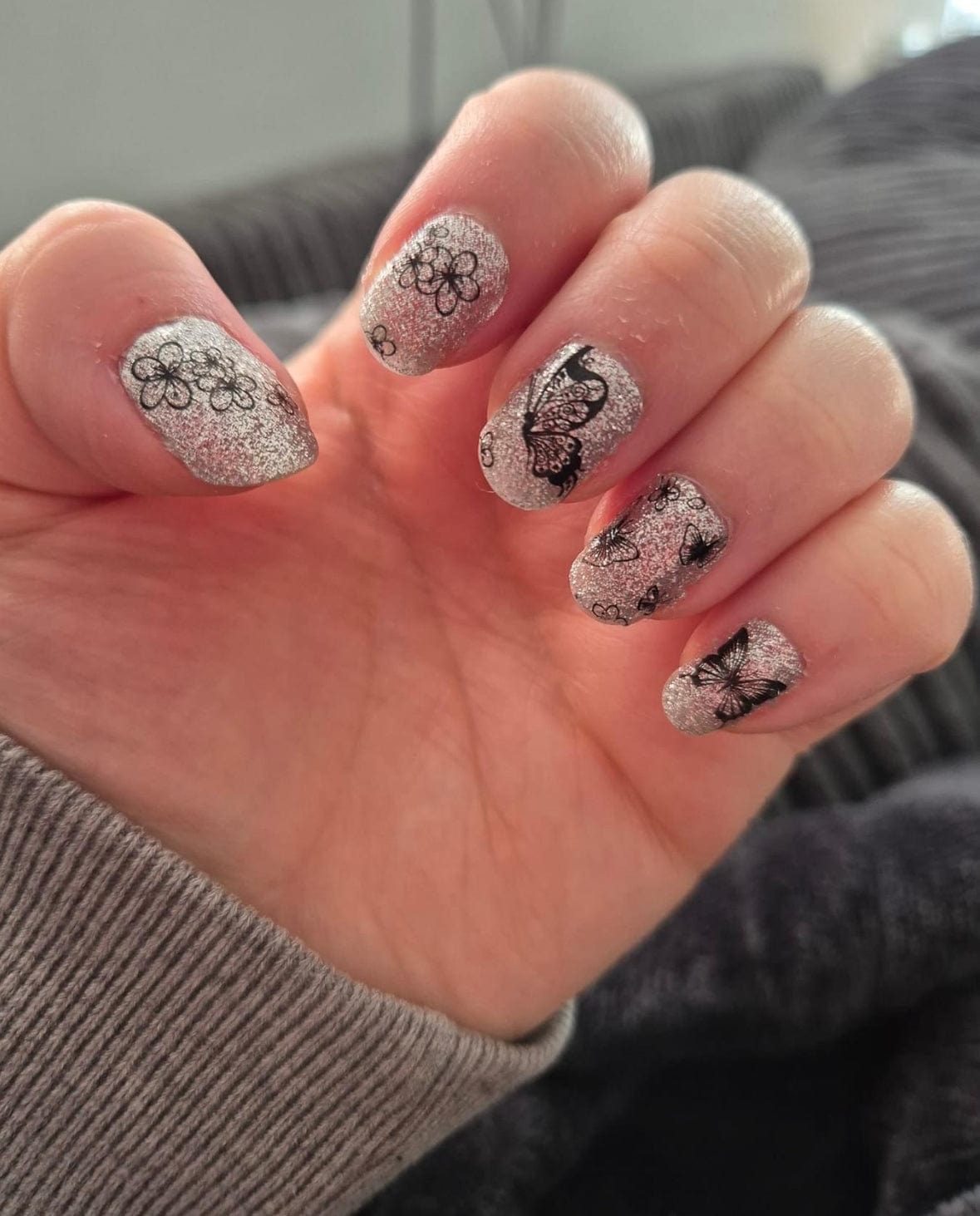 Hand wearing silver glitter gel nail wraps with black butterfly nail art patterns
