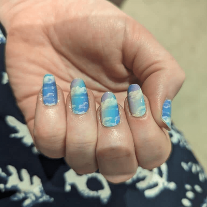 Hand wearing blue cloud nail wraps with pastel ombre gradient at-home manicure design