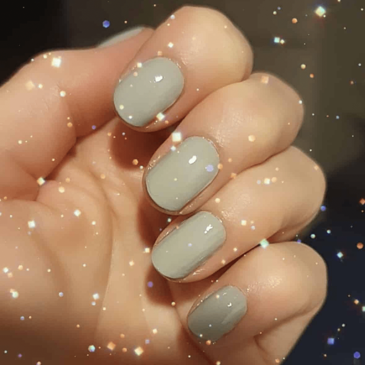 Glossy grey nail wraps on hand with sparkly background for elegant manicure look