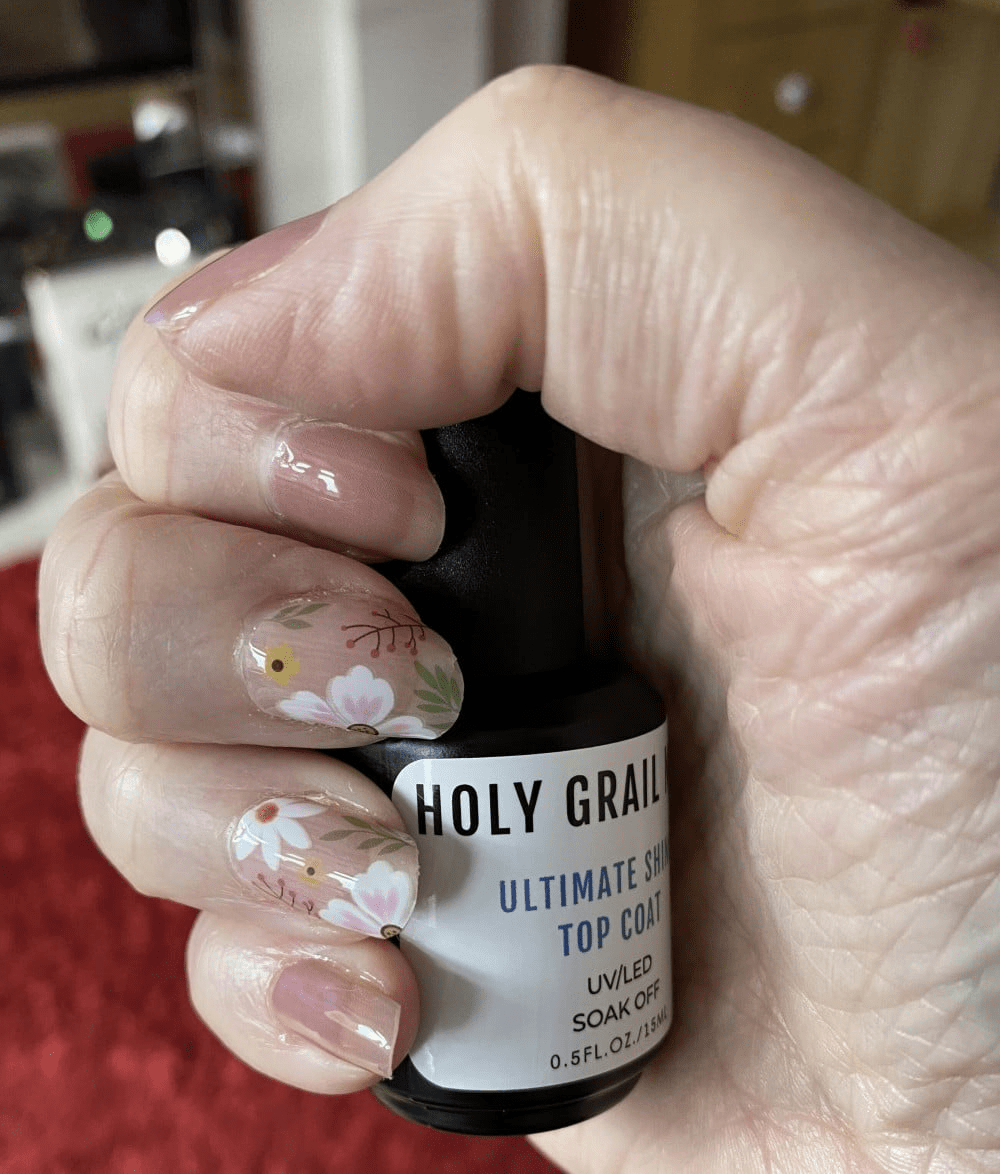 Hand holding nail polish bottle displaying white daisy floral nail wraps manicure design