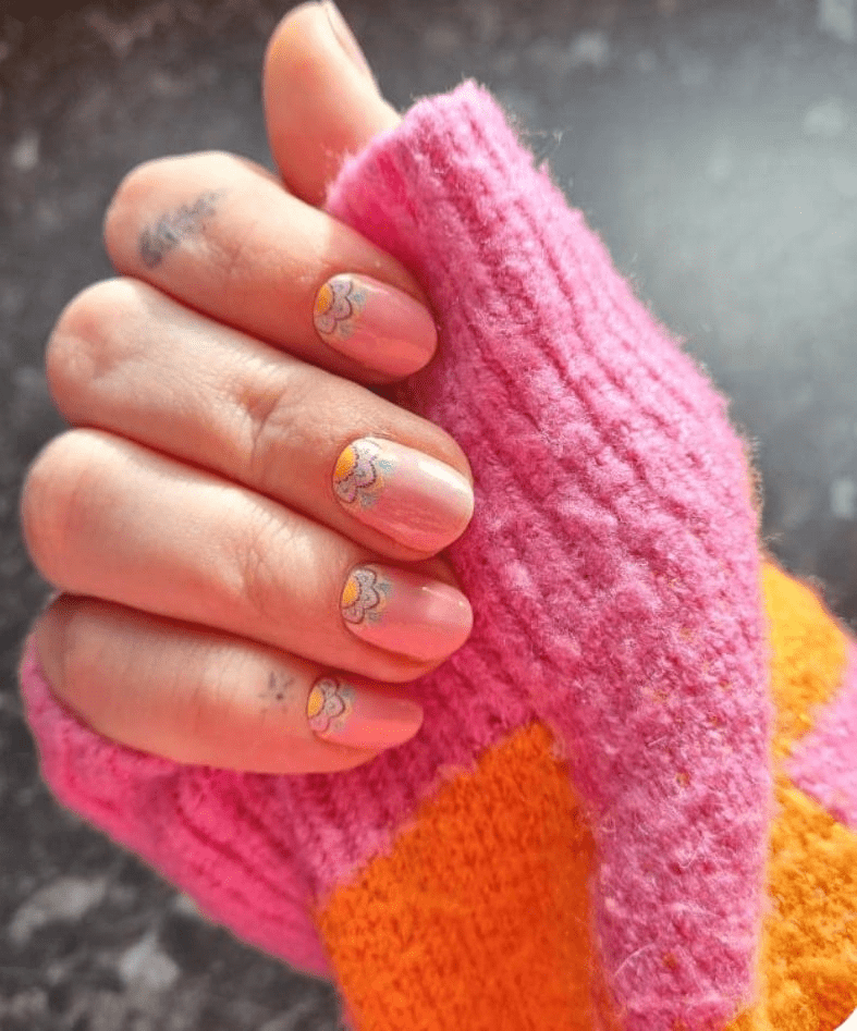 Pink daisy nail wraps on hand against colourful knitted jumper background