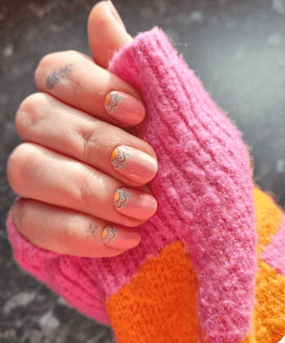 Pink daisy nail wraps on hand against colourful knitted jumper background
