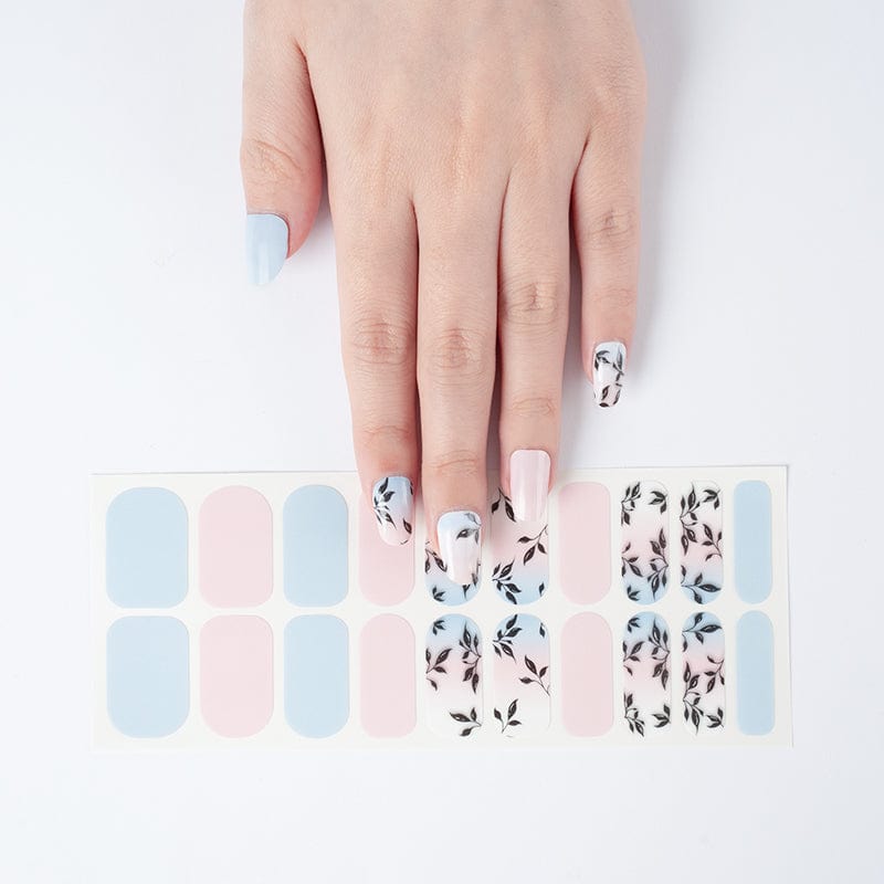 Hand wearing blue and pink nail wraps with black leaf design manicure