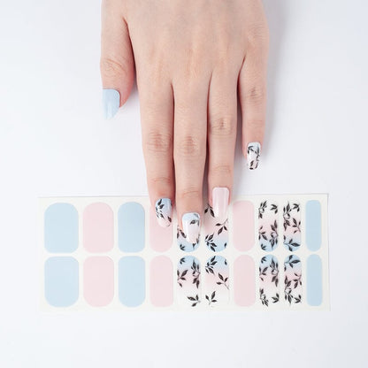 Hand wearing blue and pink nail wraps with black leaf design manicure