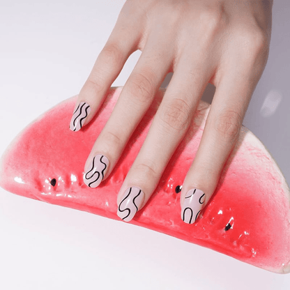 Abstract wavy nail wraps on hand holding pink watermelon slice showing monochrome nail art
