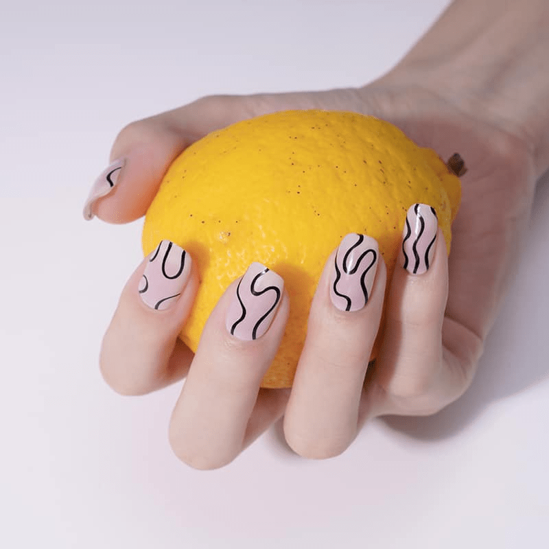 Hand with black squiggle nail wraps holding yellow lemon showing modern geometric nail design
