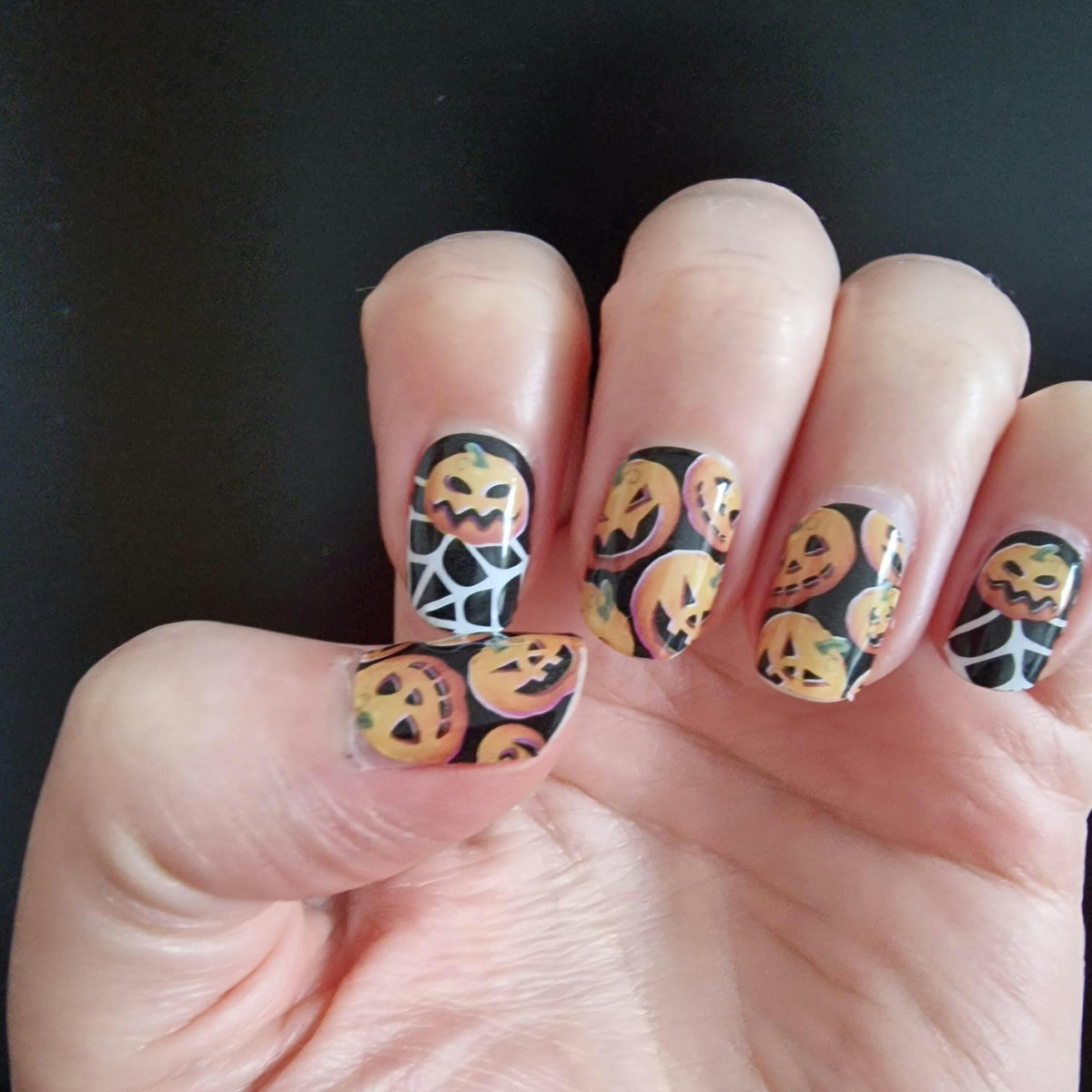 Halloween nail wraps with orange pumpkins and white spider webs on hand