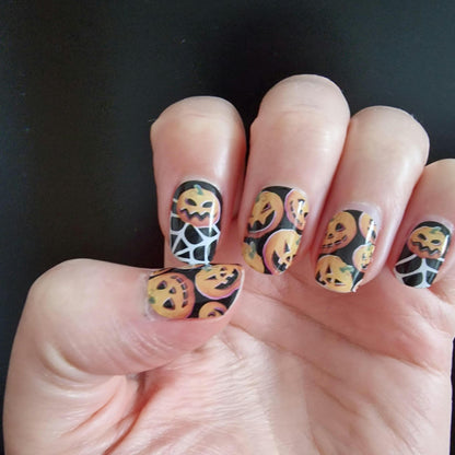 Halloween nail wraps with orange pumpkins and white spider webs on hand
