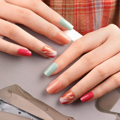 Autumn-themed nail wraps on hands featuring coral, mint green and metallic glitter patterns
