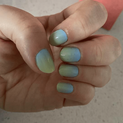Blue green colour-changing nail wraps on hand displaying multicoloured hypercolour gradient finish