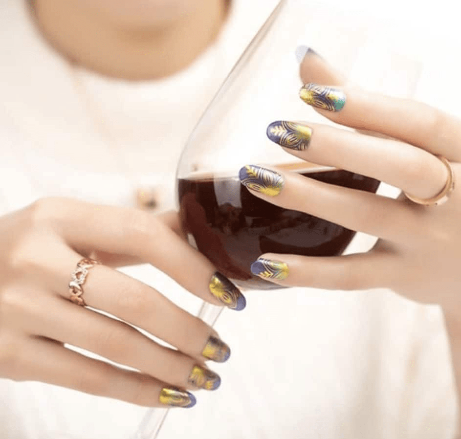 Hands holding coffee mug wearing navy and gold botanical nail wraps with ornamental lotus pattern design
