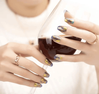 Hands holding coffee mug wearing navy and gold botanical nail wraps with ornamental lotus pattern design