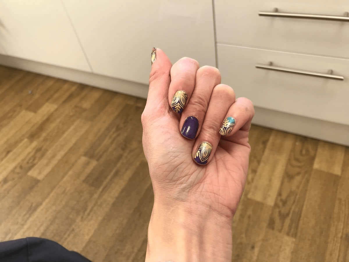 Hand displaying navy blue nail wraps with golden metallic lotus patterns for at-home manicure application