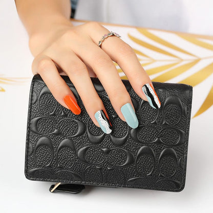 Manicured hand with geometric nail art wraps in orange blue black holding leather purse