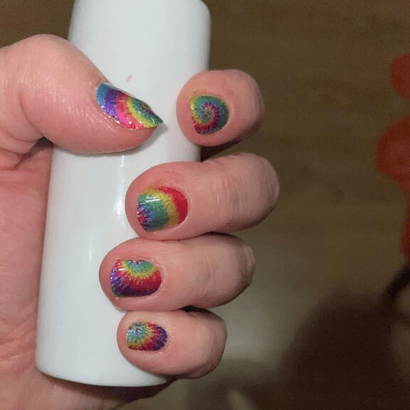 Rainbow spiral nail wraps on fingers displaying psychedelic tie-dye patterns for festival nails