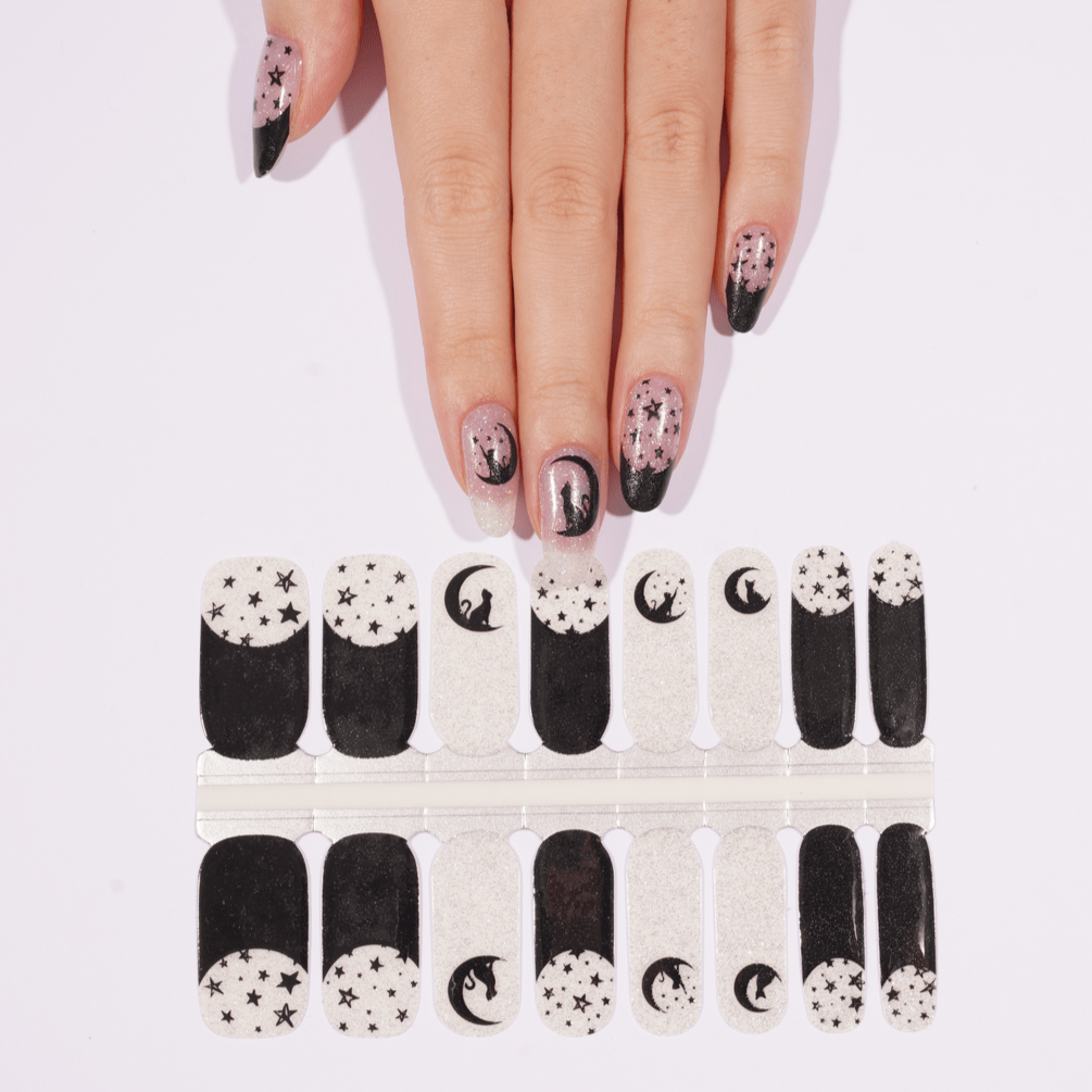 Black celestial nail wraps with silver stars and moons on hand with matching sheet