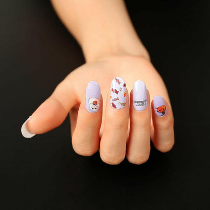Hand displaying purple and white nail wraps with cute Halloween ghost and pumpkin designs