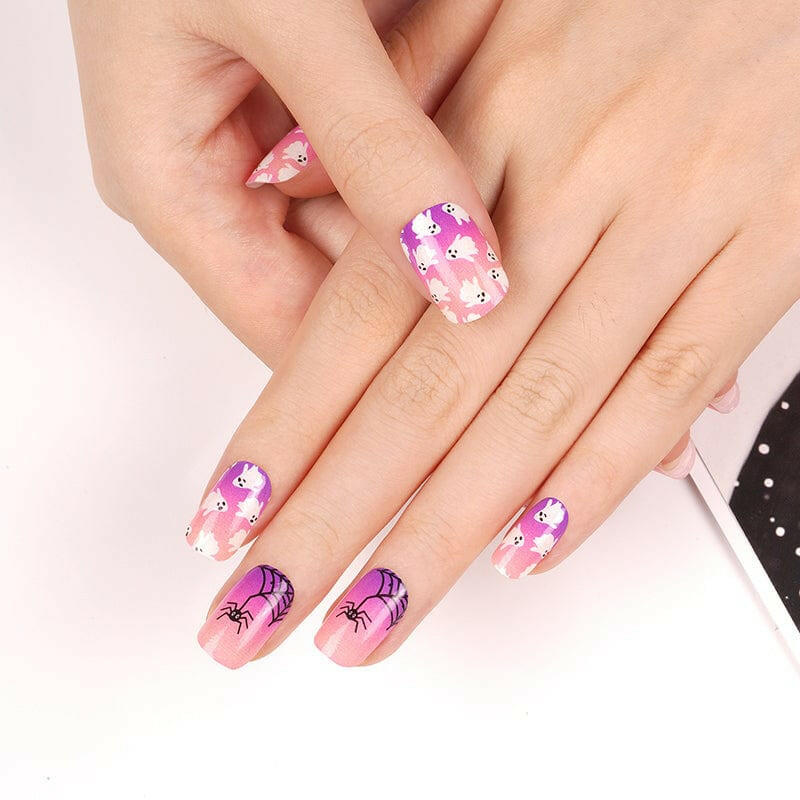 Pink and purple Halloween nail wraps with skulls and spiders on hand manicure