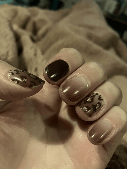 Hand displaying brown leopard print nail wraps with nude accent nails and glossy finish