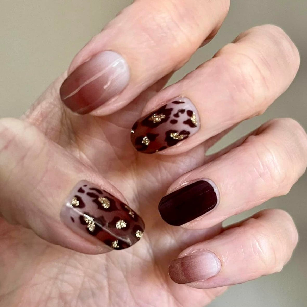 Brown leopard print nail wraps on hand with glossy finish and gold accents