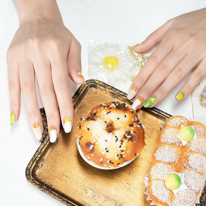 Hands with colourful citrus nail wraps featuring orange and lime designs over breakfast setting