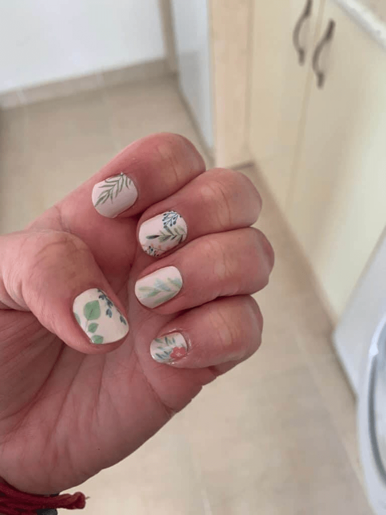 Hand displaying cream floral nail wraps with botanical leaf and flower patterns