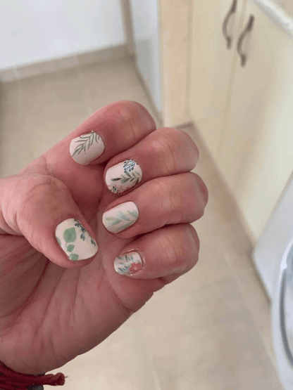 Hand displaying cream floral nail wraps with botanical leaf and flower patterns